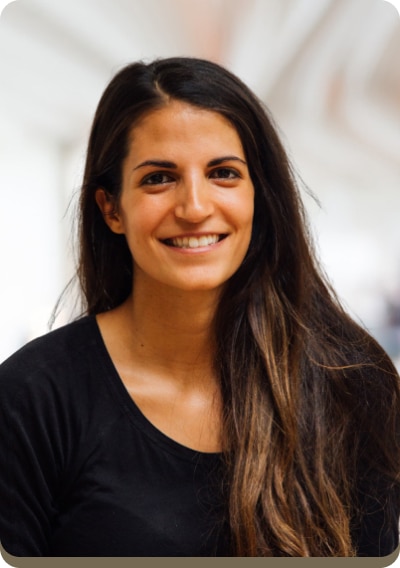 Person with long, dark hair smiles while wearing a black top; blurred background.